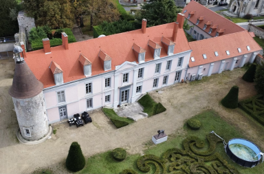 Château avec toit rouge, tour ronde et jardin soigné.